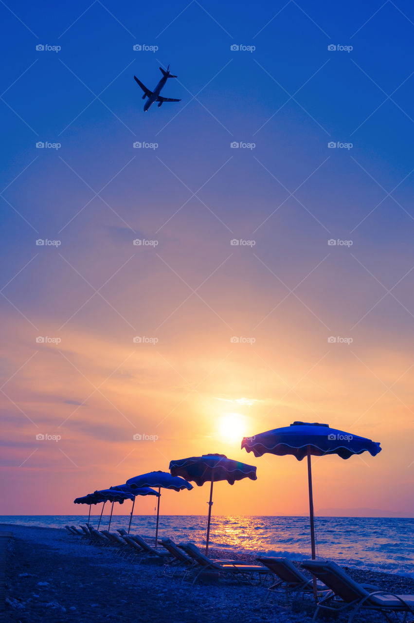 Airplane flying above beach umbrellas.