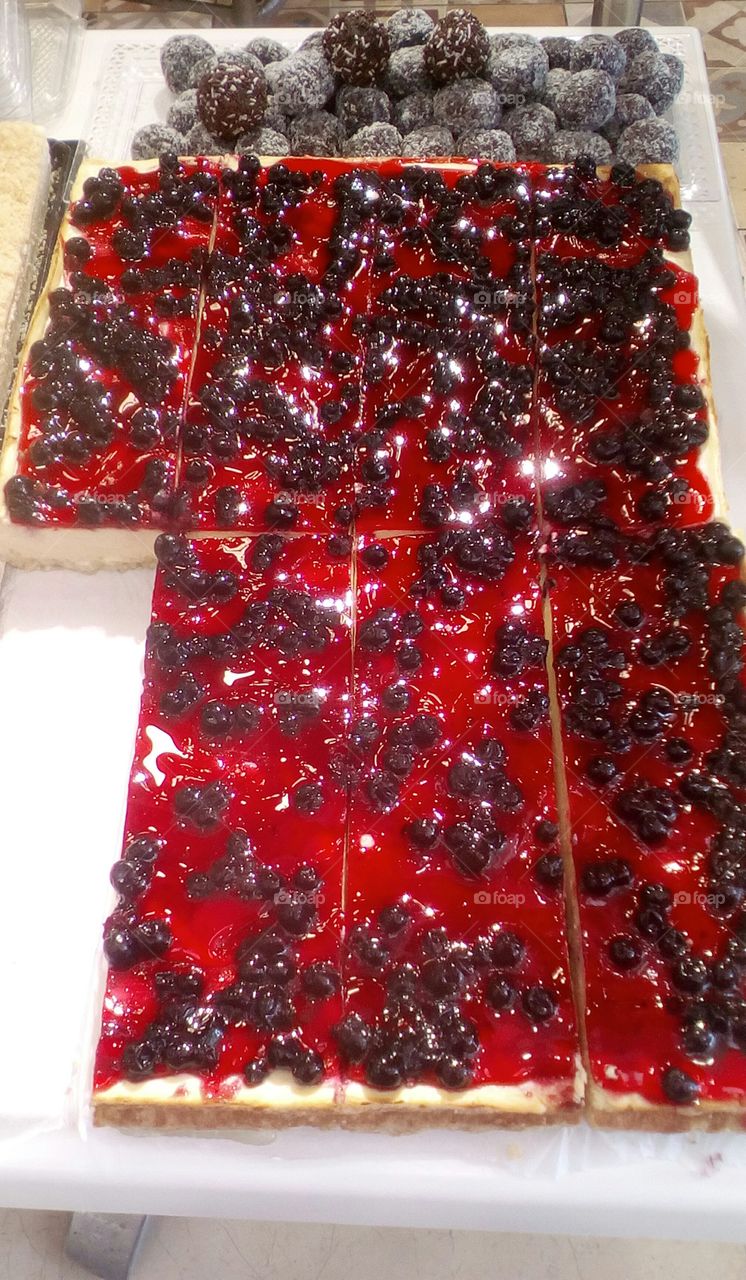 Long and large delicious cake with fruits 
glazure in bakery.In the backround are 
many delicious chocolate ball-shaped