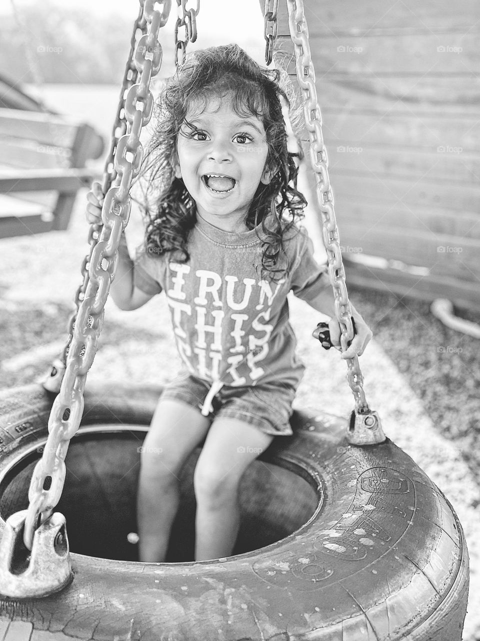 Toddler girl swings on tire swing at playground, black and white portrait, toddler on the playground, toddler girl has fun on the playground, tire swings at the playground, fun outside in the summertime 