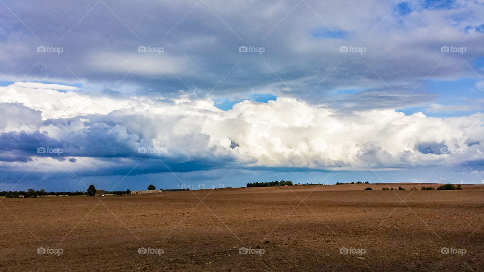 Große Wolke über einem Acker, im Hintergrund Windräder.