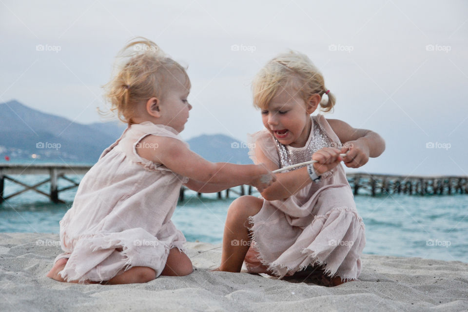 Two sisters on the beach fighting for a stick. Majorca Spain.