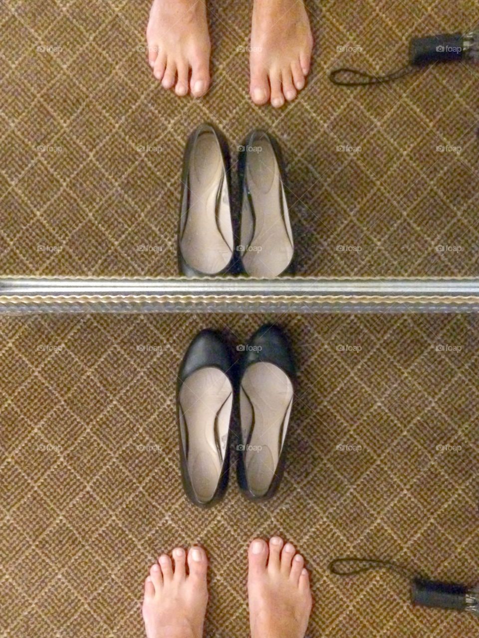 Female feet, shoe selfie, reflection in mirror, umbrella on floor. The last step to getting dressed, putting shoes on. However, these female feet hesitate to wear heels in the rain.