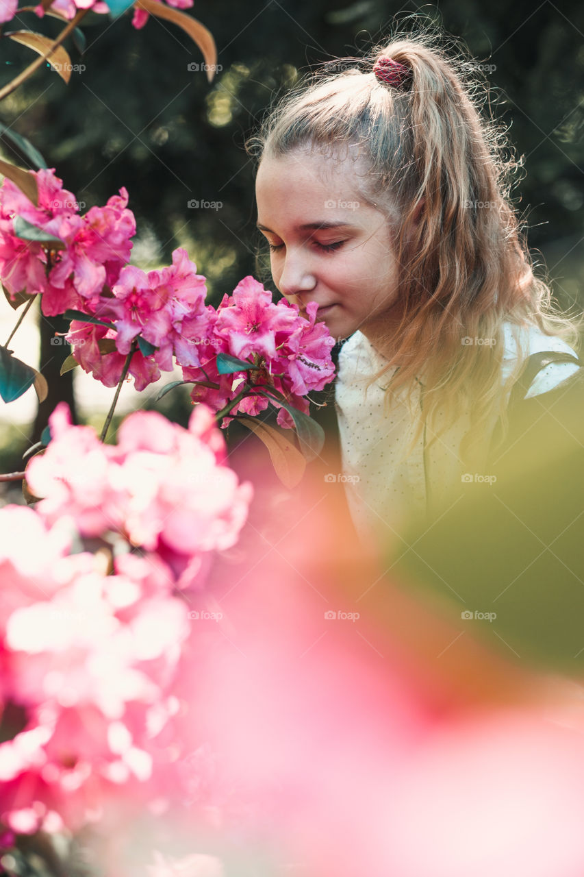 Girl with closed eyes standing in garden among the flowers, smelling beautiful pink flower