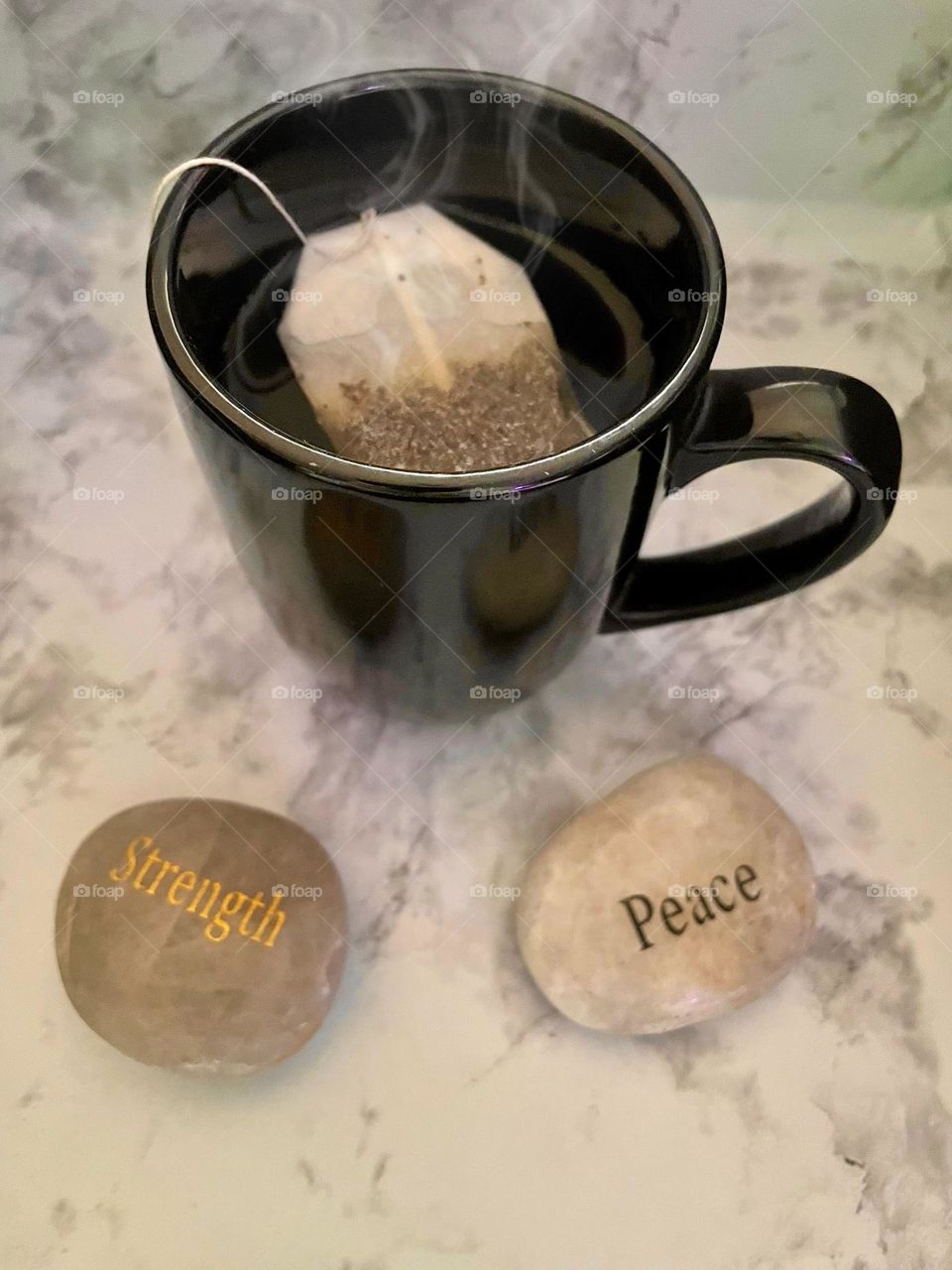 A strong cup of tea steeps with rocks stating strength and peace on a marble background