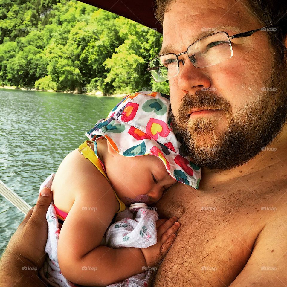 Dad holding his sleeping baby girl on a bright summer day out on the boat