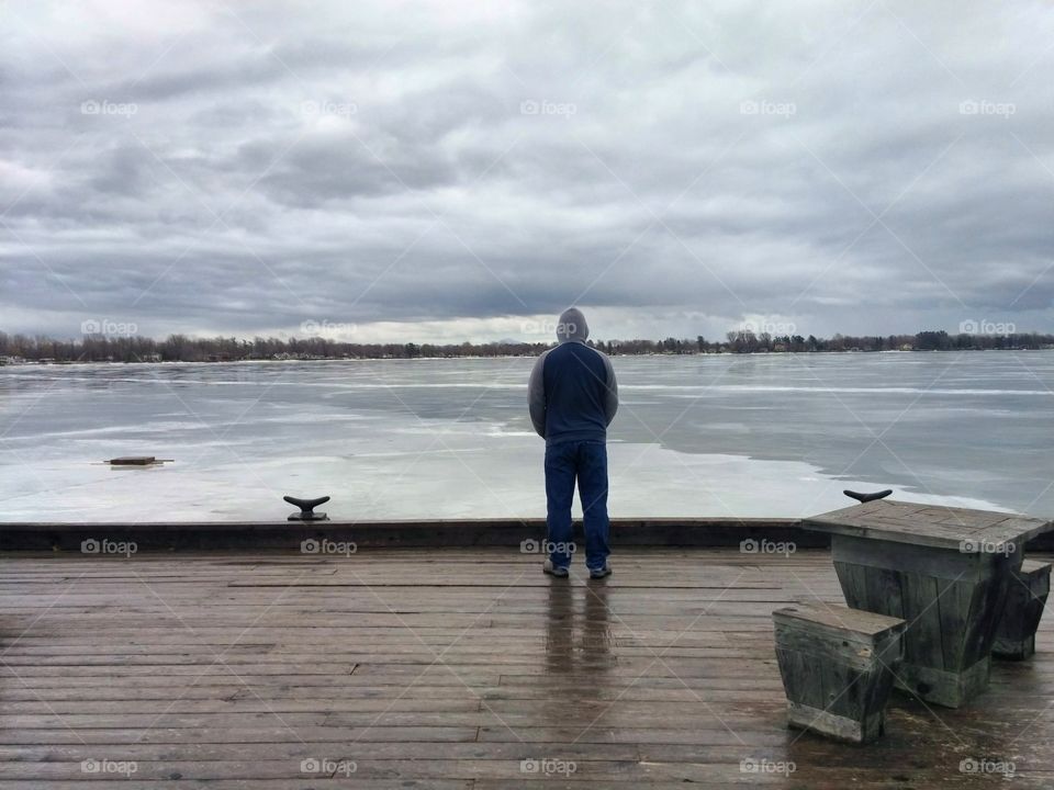 Man stands looking over a frozen landscape from a wooden boardwalk.