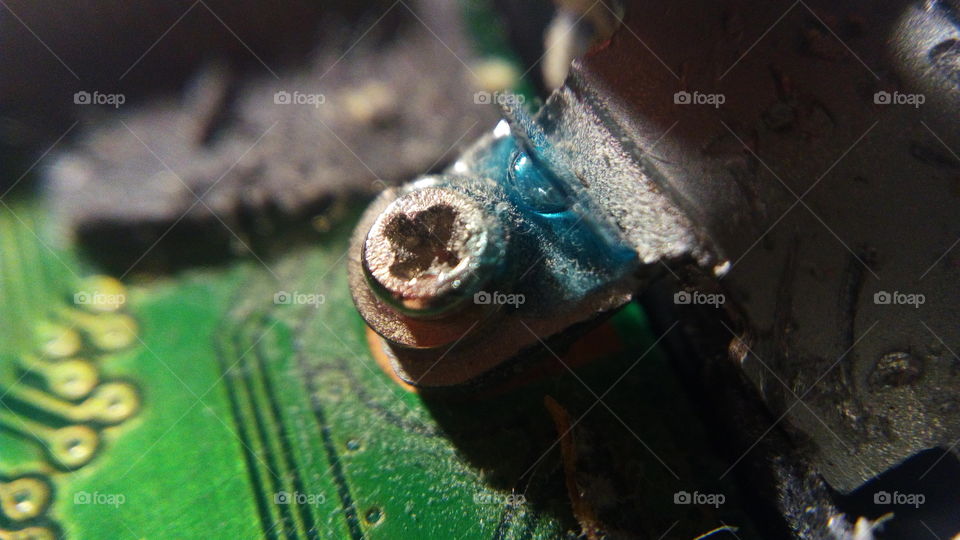dusty screw on a microcircuit with a drop of blue glue (macro photo)