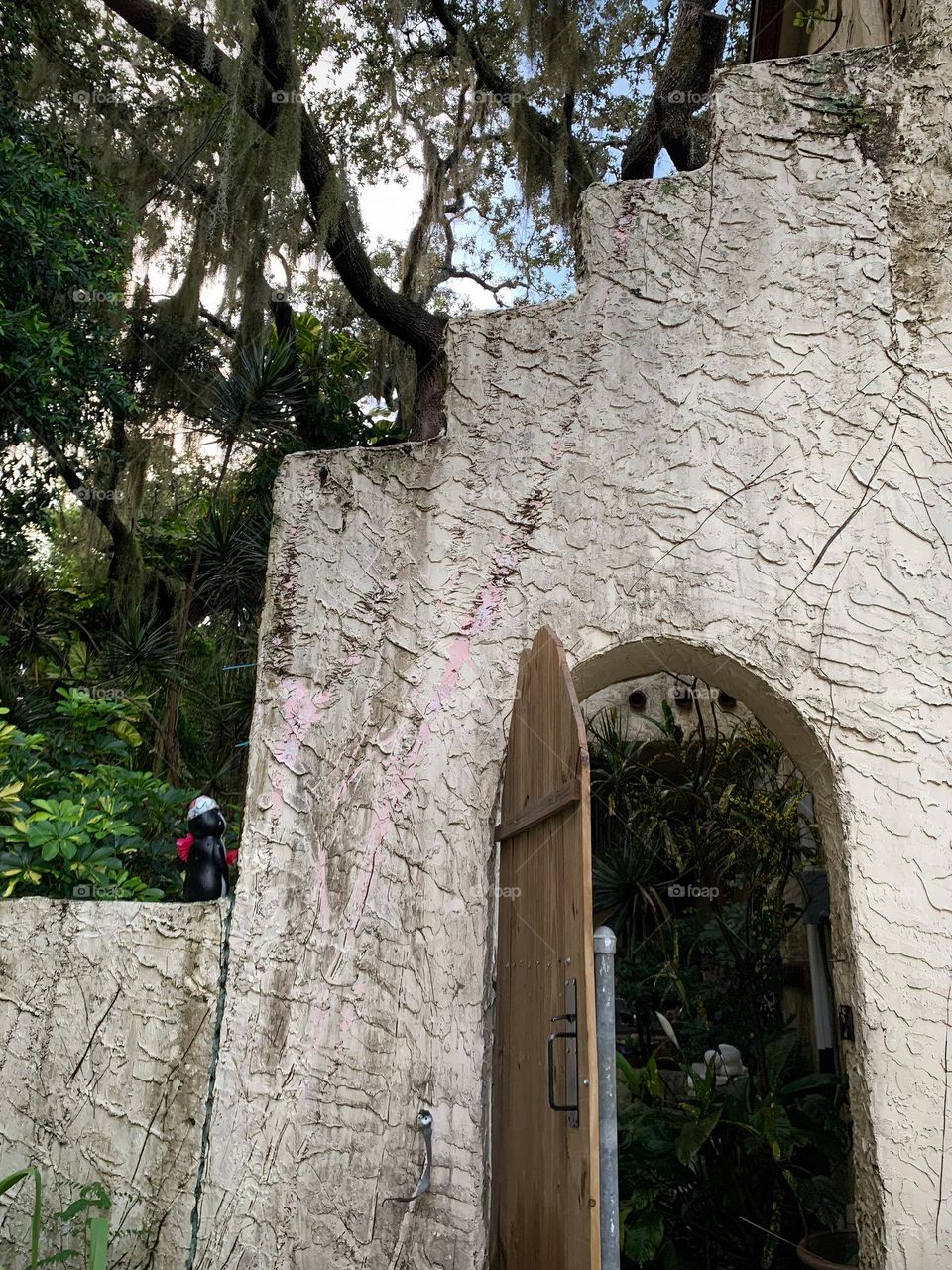 White and red spanish old style architecture residential large house built in the early 1900s. Doorway with antique style wood door in a stairway wall seen from tropical plants and live oak trees leading to another garden.