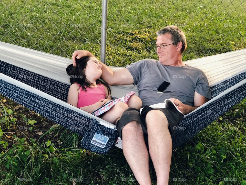 Father and daughter relaxing in hammock and reading