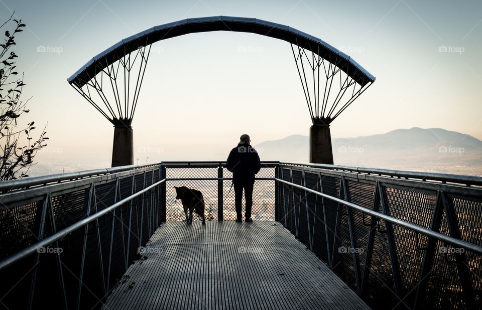Man walking dog on viewpoint. Silhouette of a man walking a dog onto a viewpoint overlooking a valley.