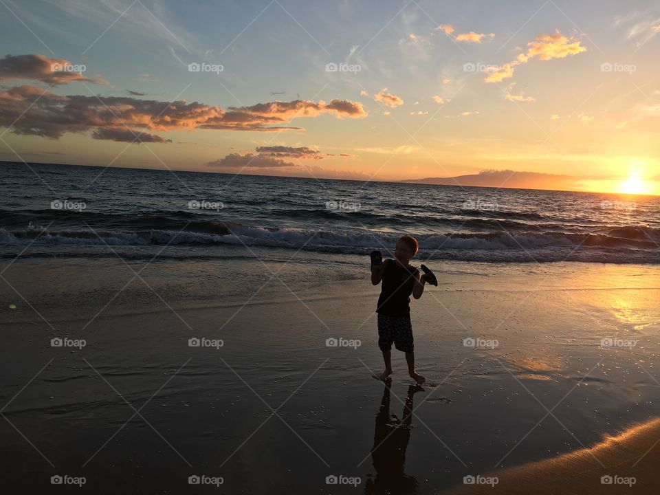 Kid is silly pose silhouetted against breathtaking Hawaii sunset 