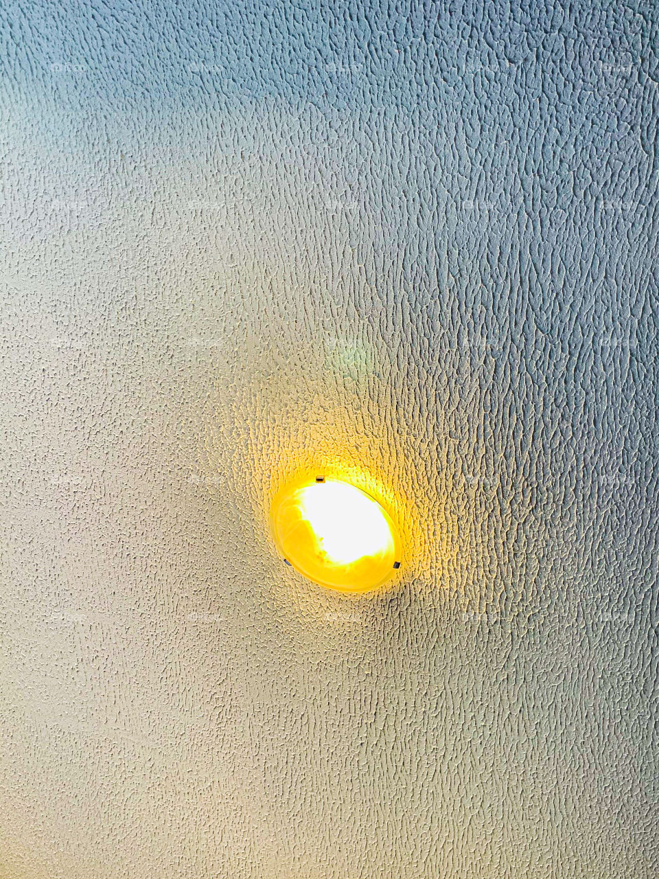 A bright shining round bulb lighting a grey rough textured concrete roof wall. 