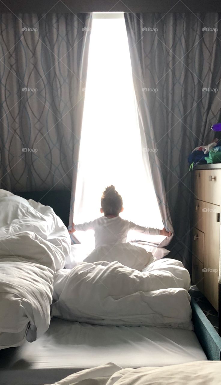 Summertime is vacation time... little girl waking up and opening the curtains on a cruise