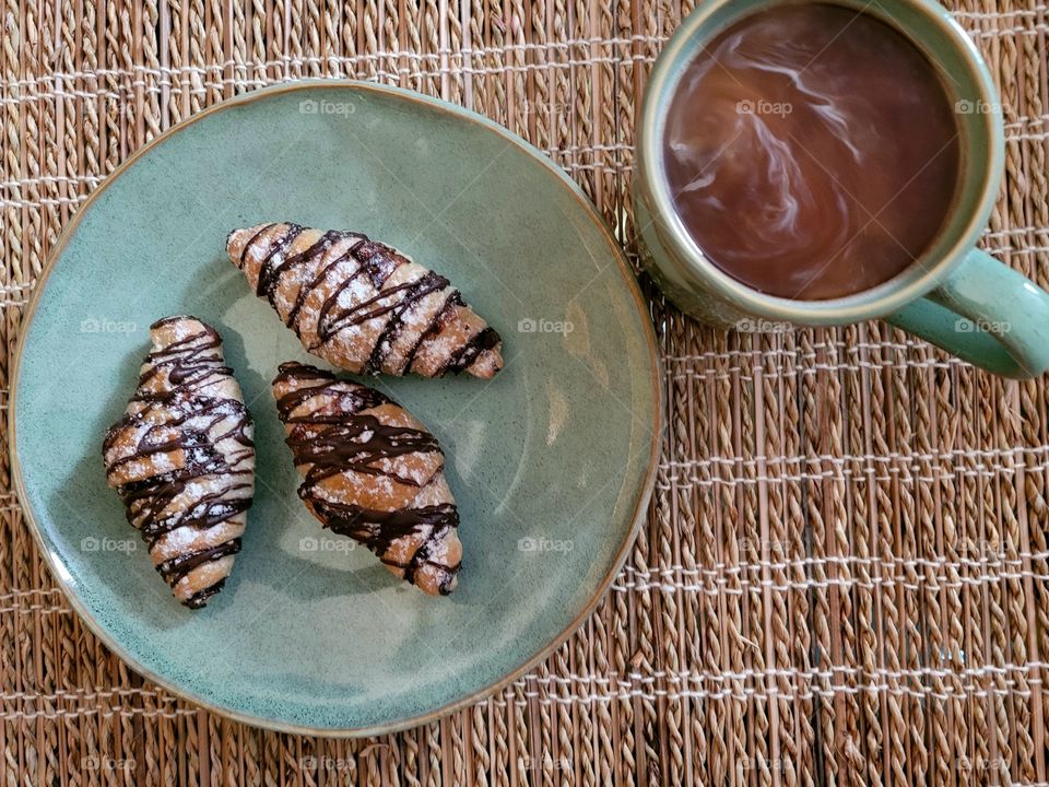 Morning time, simple breakfast of chocolate croissants and coffee on bamboo placemat