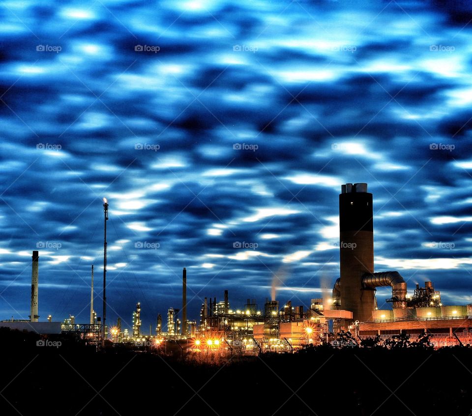 An industrial oil refinery lit up at night under an unusual cloudy sky.