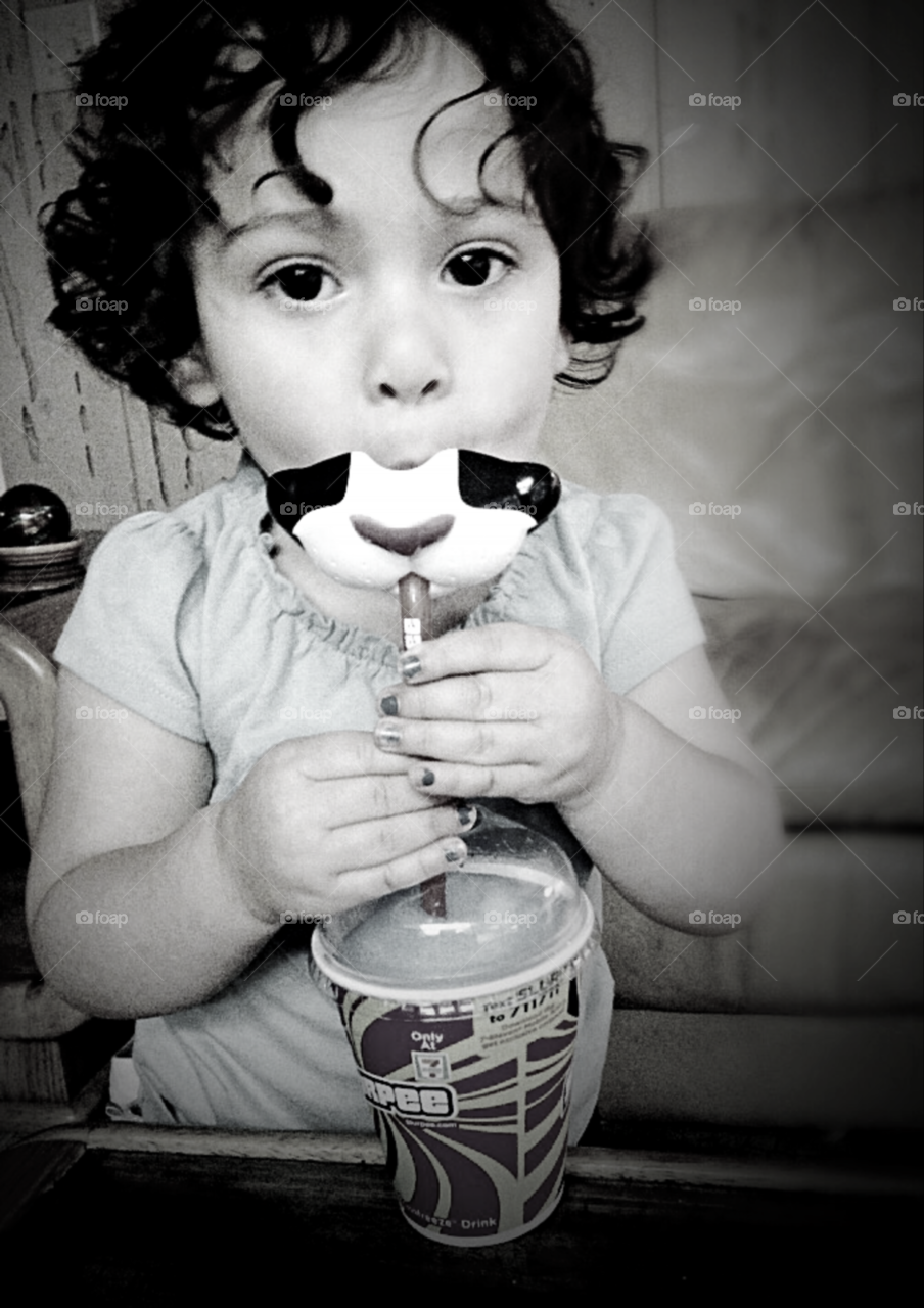 Little girl with curly hair, big eyes, and chipped nail polish drinks out of cat mouth straw 
