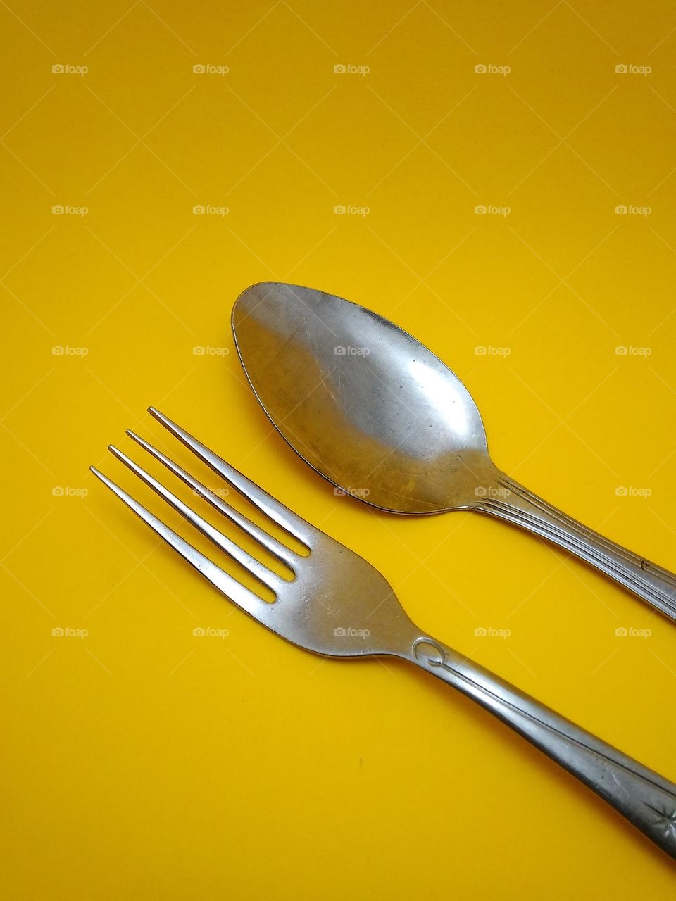 cutlery spoon and fork made of stainless steel in the photo in the studio on a yellow background.