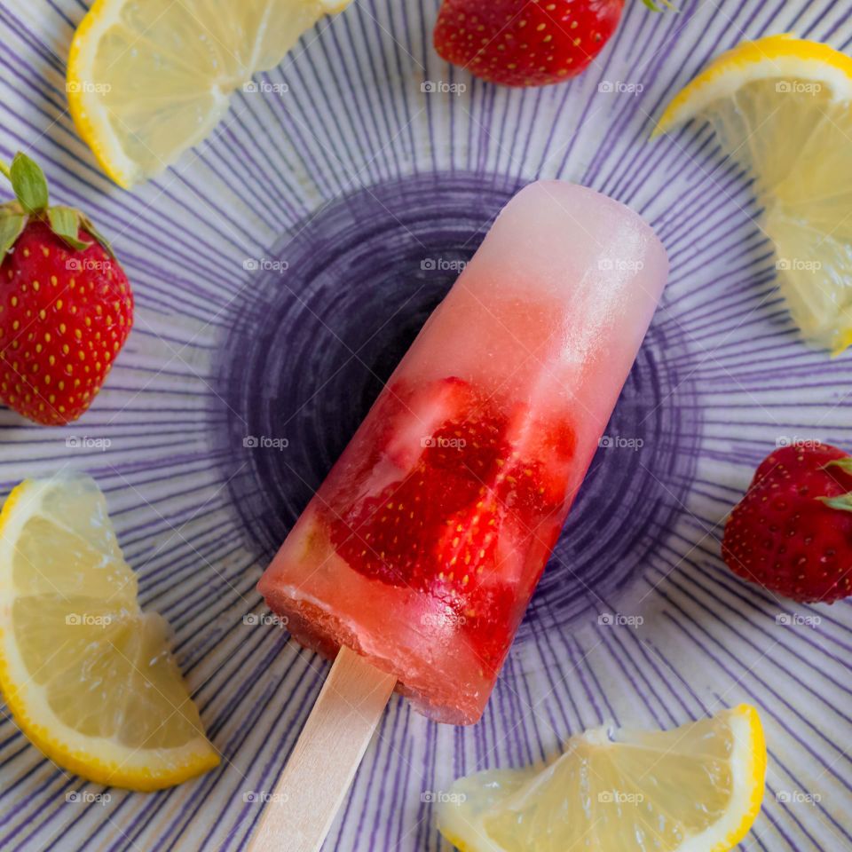 Strawberry and lemonade ice lolly displayed on a plate with fruit pieces 