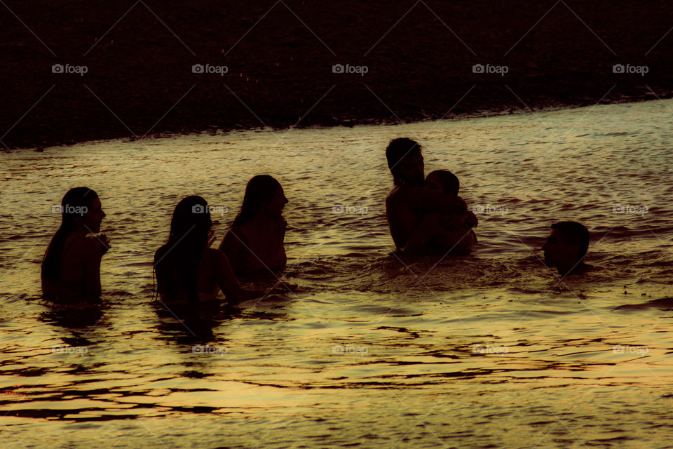 Young people having fun in the river, they are silhouetted against the water