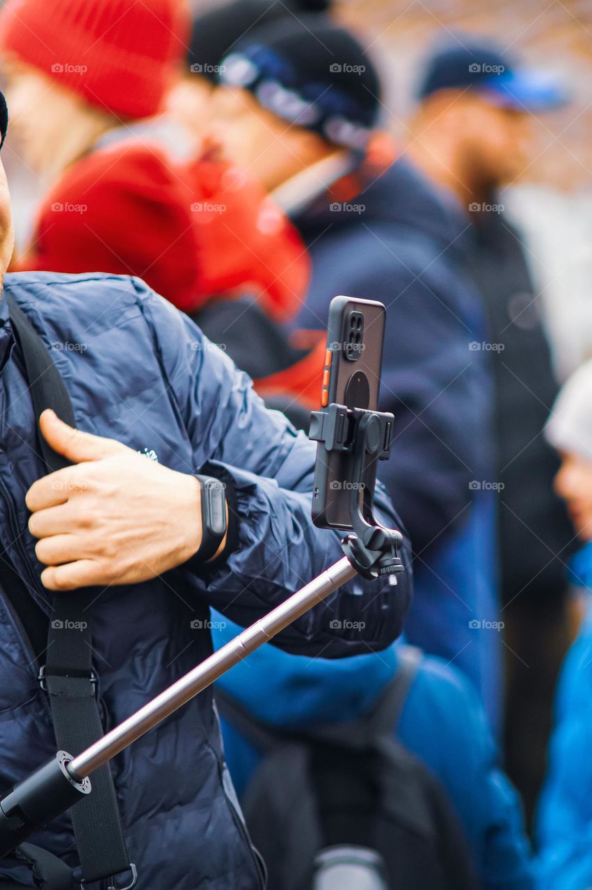 The guy takes a photo on a smartphone and uses a selfie stick