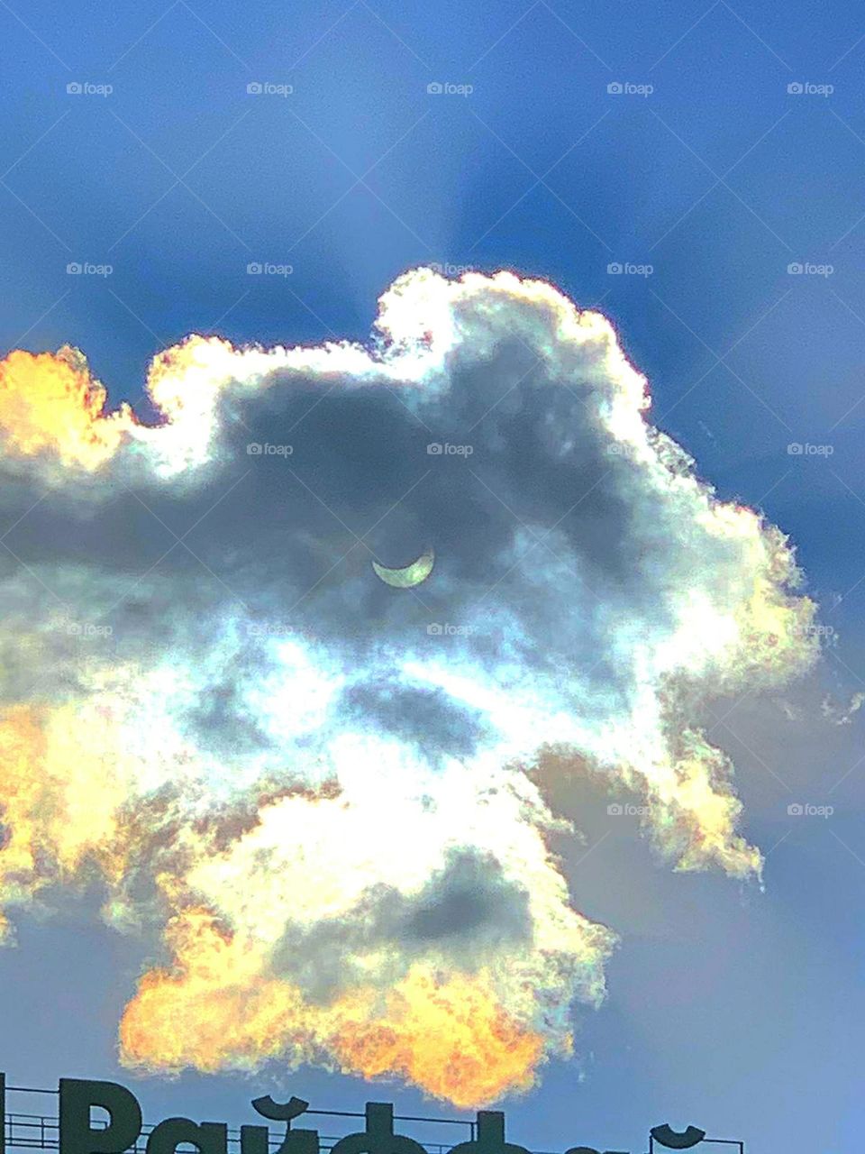 Cloud. Solar eclipse. Through the cloud you can see the sun, which the moon covered by 70 percent. The remaining sun spreads its rays and colors the blue sky and cloud