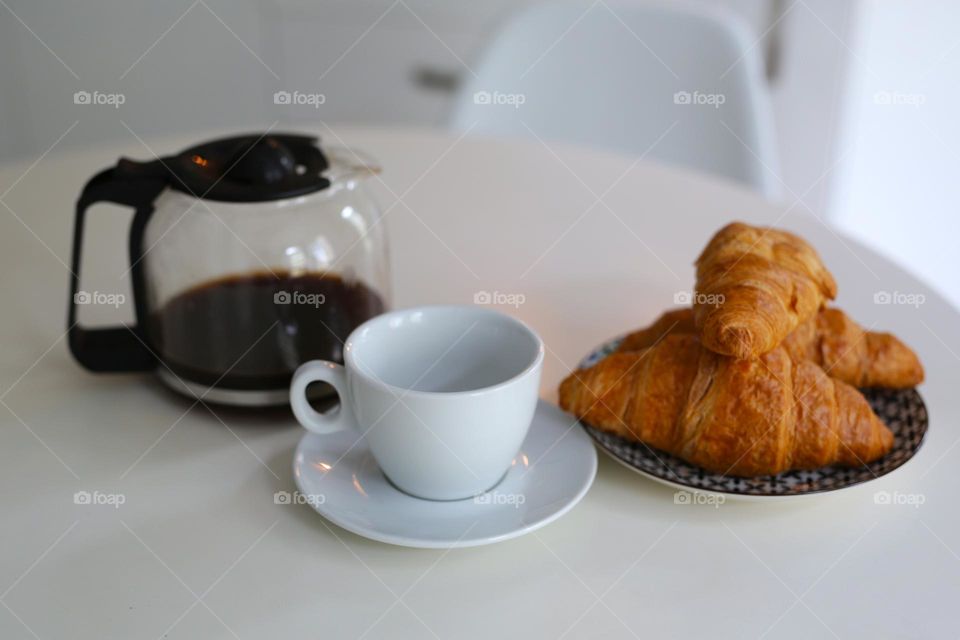 morning, on the table is a coffee pot, a cup and fresh croissants.