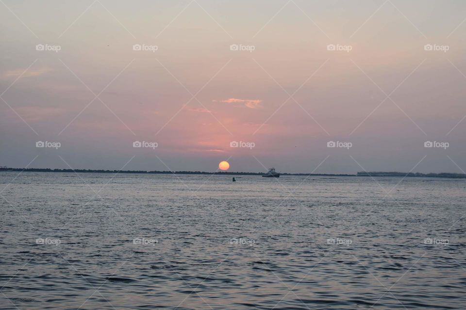 Pastel sunset over the beach in Destin, Florida. The sun is small in the distance. Boat silhouettes on the horizon.
