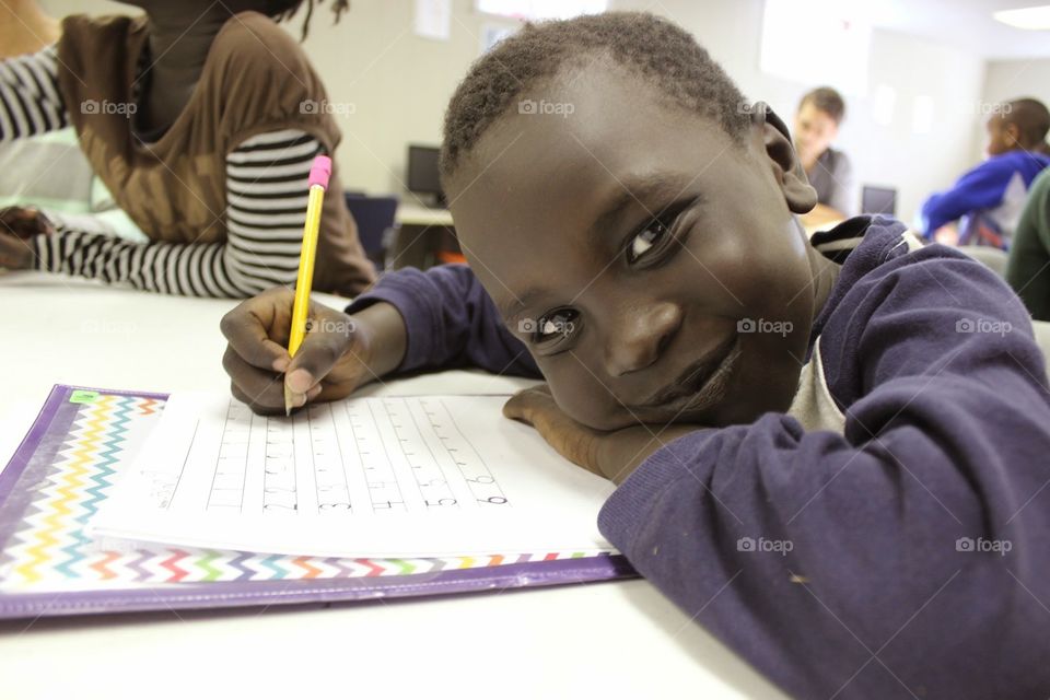 boy learning. a young refugee student practices writing his letters in an after school tutoring program