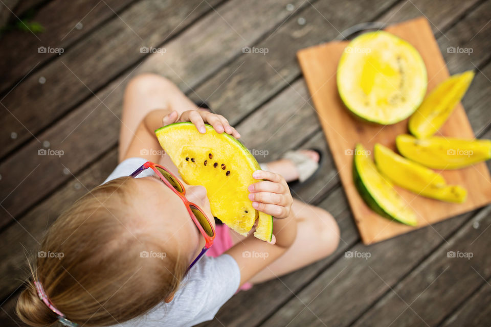 Little girl with blonde hair eating yellow watermelon outdoor 