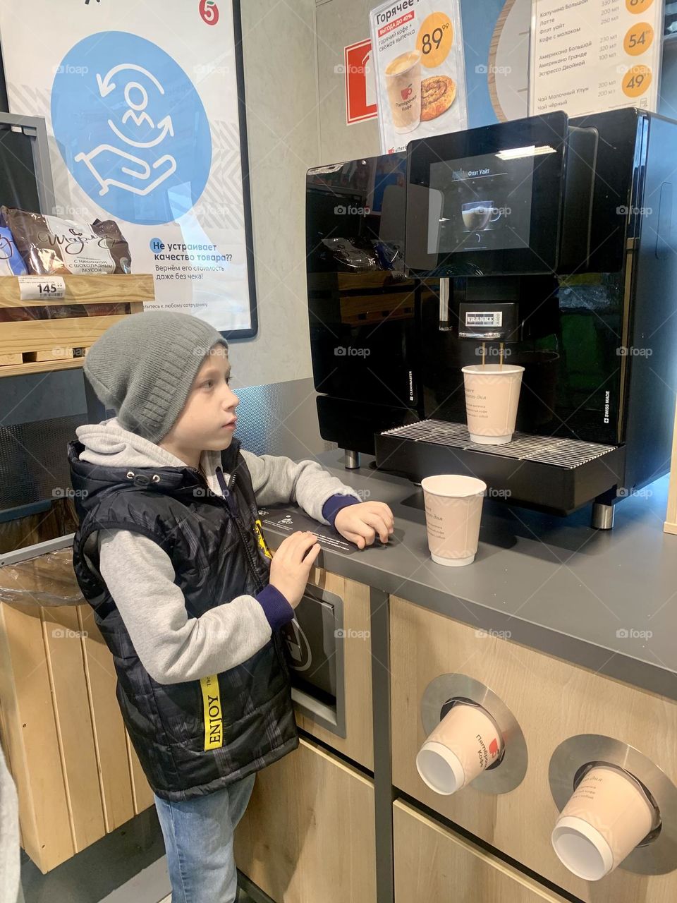 The boy is waiting for coffee from the avitomat in the store