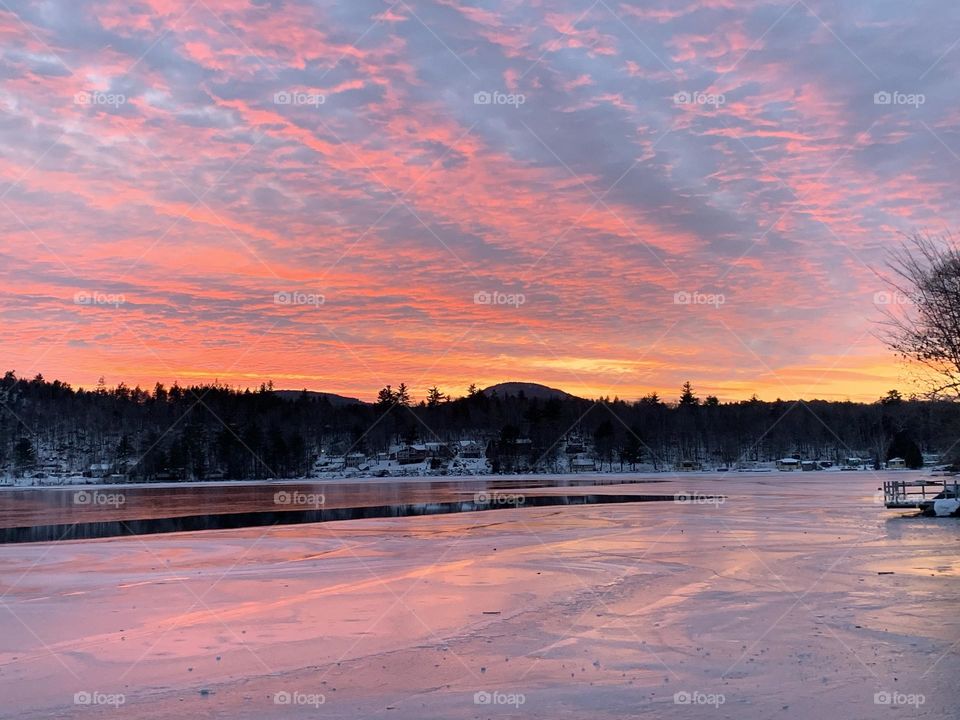 Patience, resilience, and the beauty of stillness - Capturing the magnificence of a beautiful sun as it rises from behind the mountain and forest, then paints the sky and the surface of the partially frozen lake with a kaleidoscope of colors. Maine