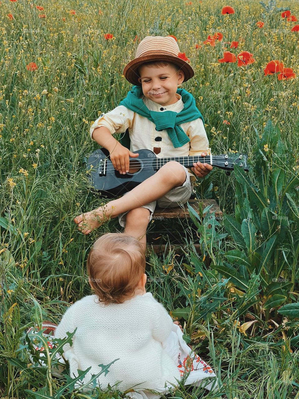 A toddler playing on the guitar and a little girl listening between flowers