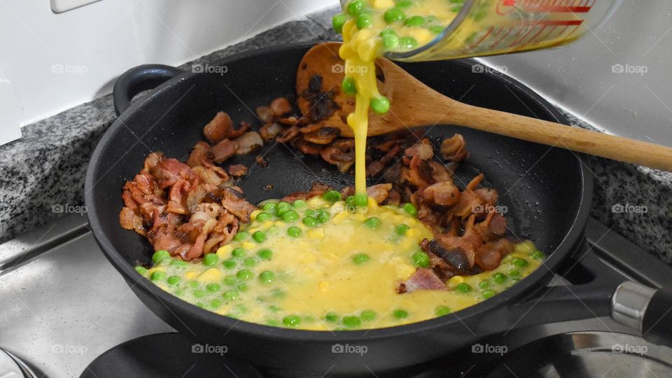 Homecooking cooking Frittata at home and adding and mixing ingredients and removing the Frittata from the pan for cutting and serving on a white plate with tomatoes. Healthy home cooking in kitchen. Breakfast and lunch food preparation.