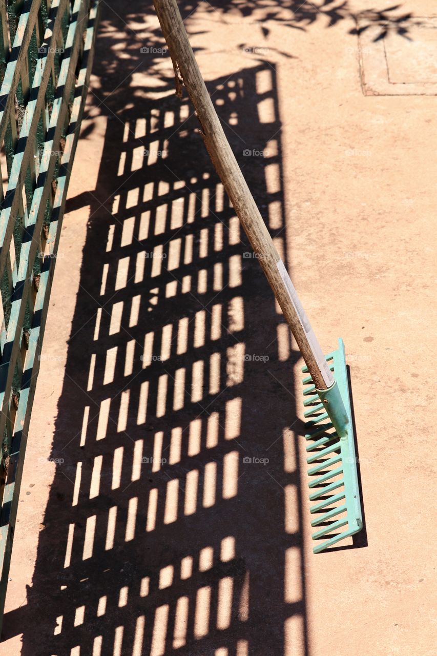 Shadow play from green lattice outdoor wood fence and garden rake in backyard 