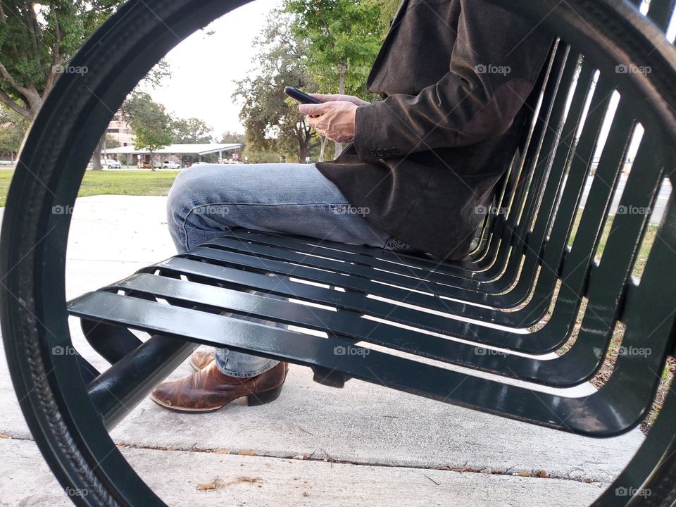 Man sitting on metal bench on phone