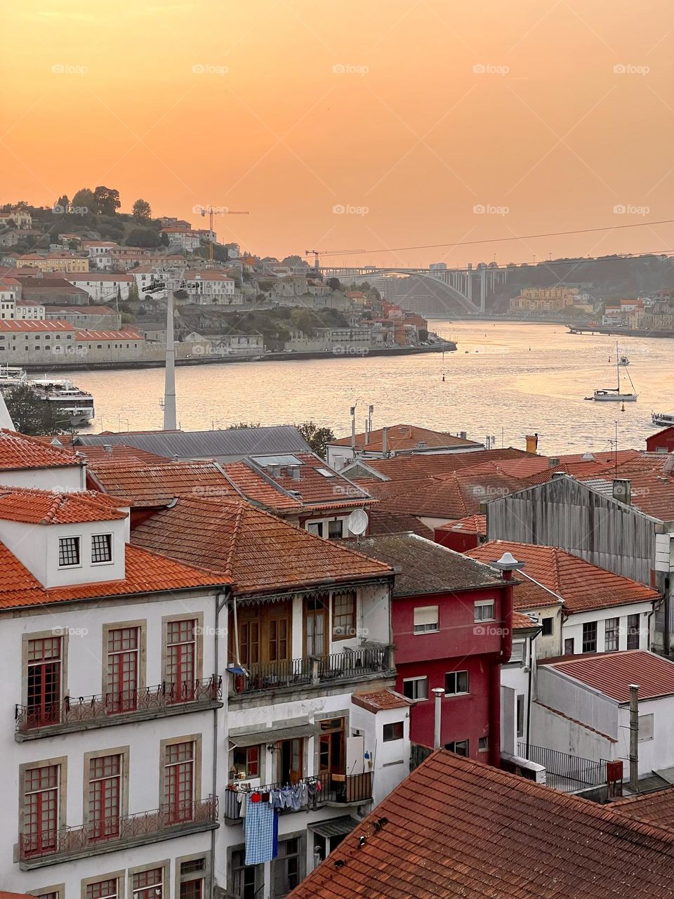Sunset over Porto rooftops, laundry on a balcony, and Rio Douro bridge in view