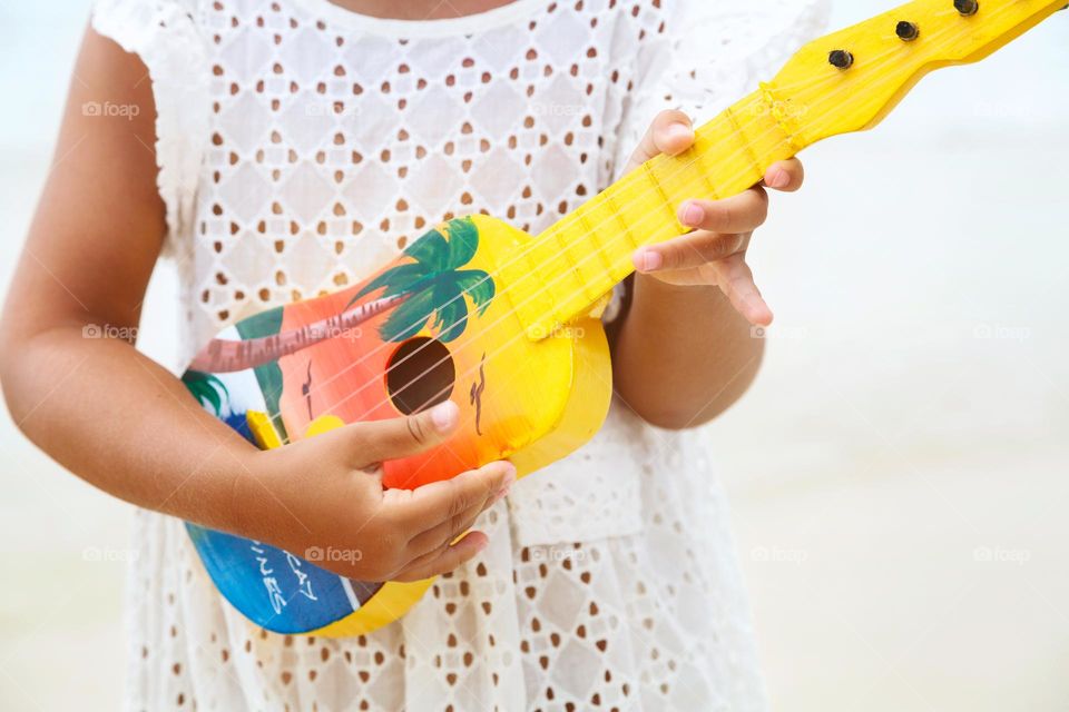 Little Caucasian girl playing on small guitar on beach 