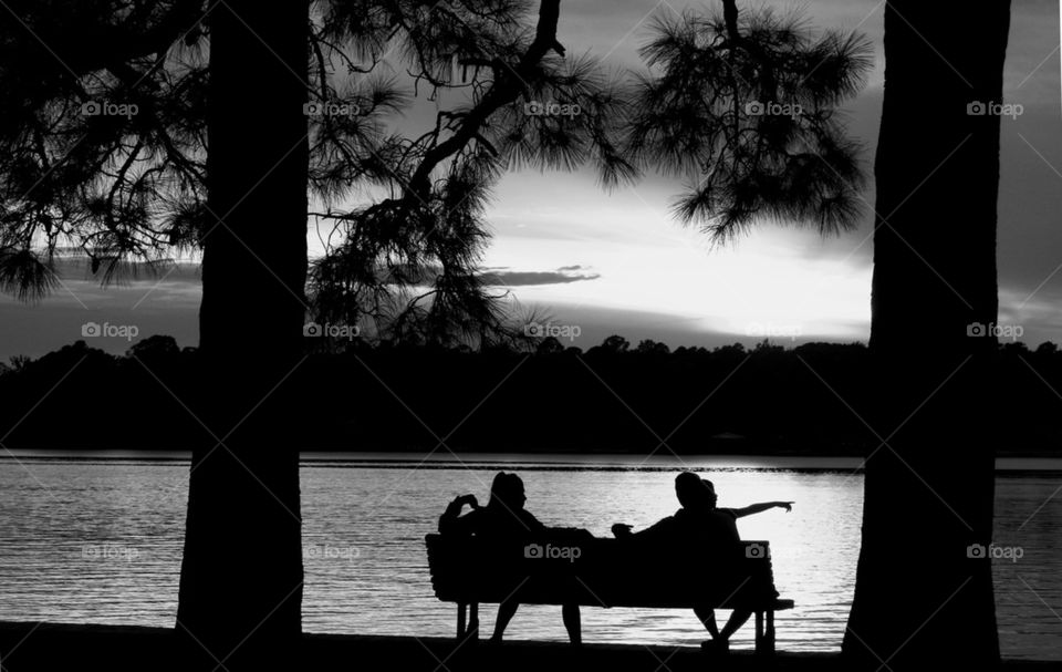 Silhouette of people sitting on bench near lake