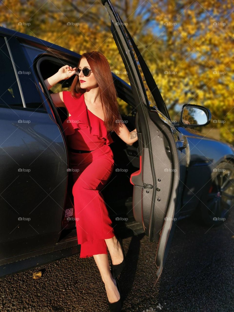 Beautiful woman with long hair in a red outfit look around from the car. Autumn time...