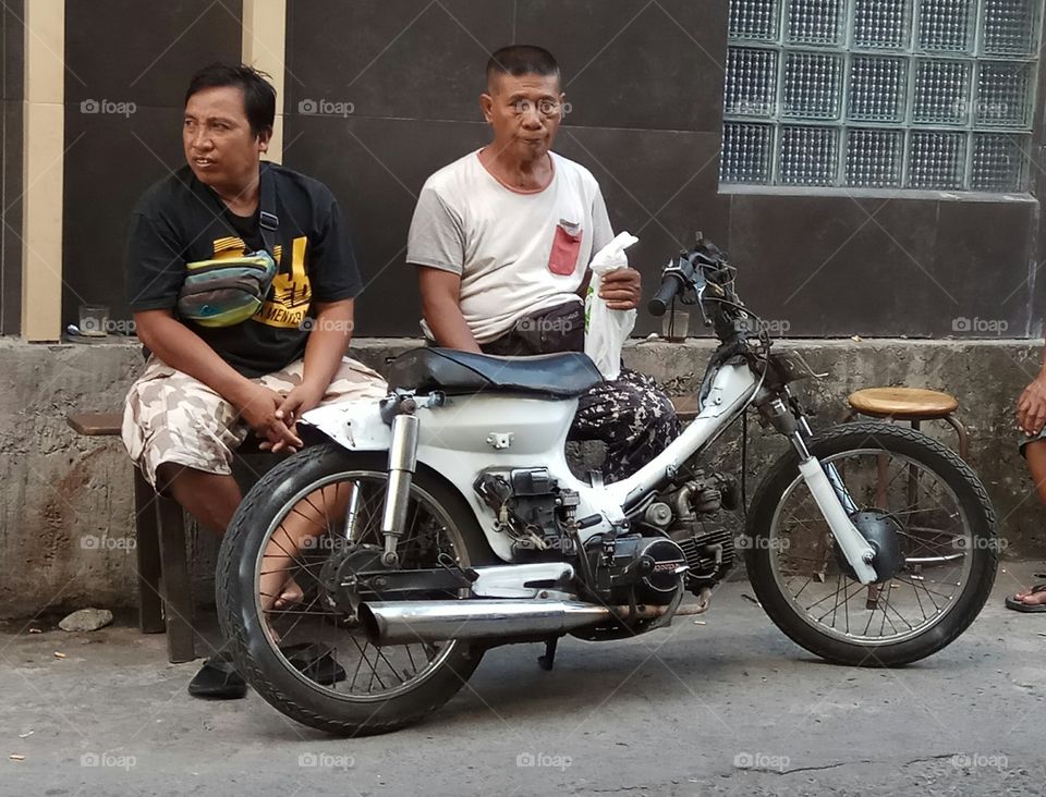 Mature men sitting on bench in front of motorcycle