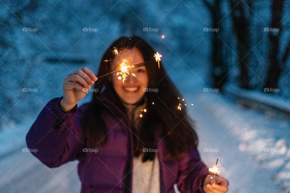 Happy woman holding sprklers in her hand, while being on road covered in snow.