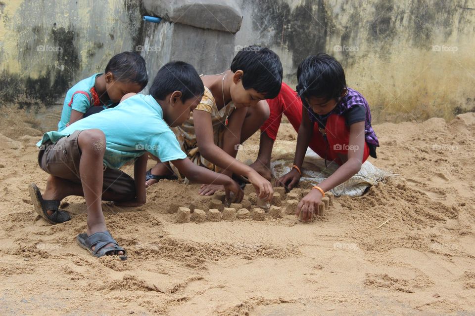 This picture describes four little children playing with fun and making cake in sand.