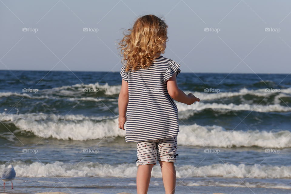 little cute girl with curly hair looks at the waves of the Baltic Sea „Heringsdorf Germany“ 