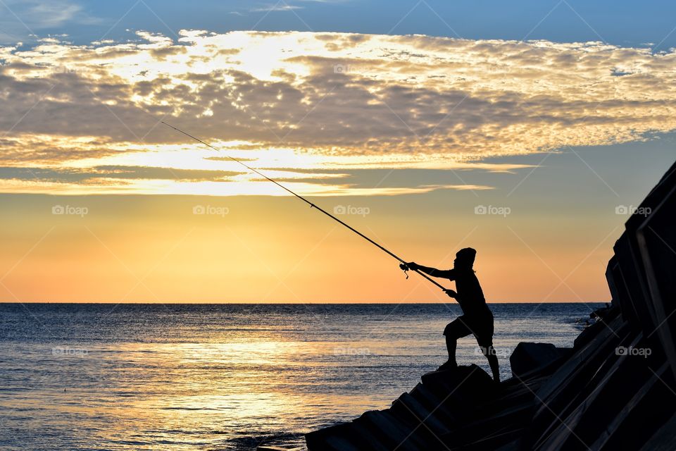 a fisherman is swinging a fishing rod during the golden hour on the edge of the port of Probolinggo