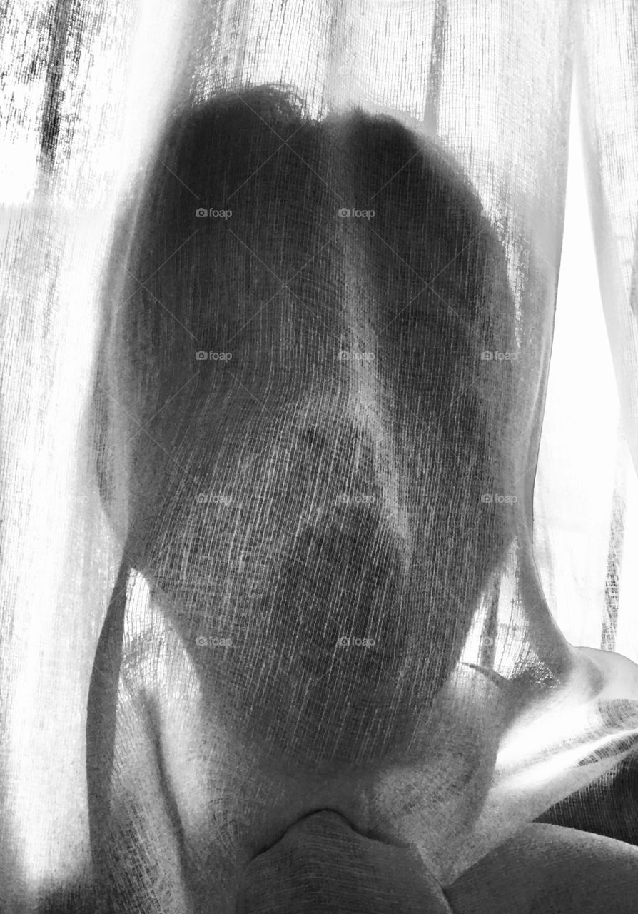 The model is behind a curtain with her mouth and eyes wide open. The idea of ​​photography is to look like a ghost or something similar to a ghost that is very scary.