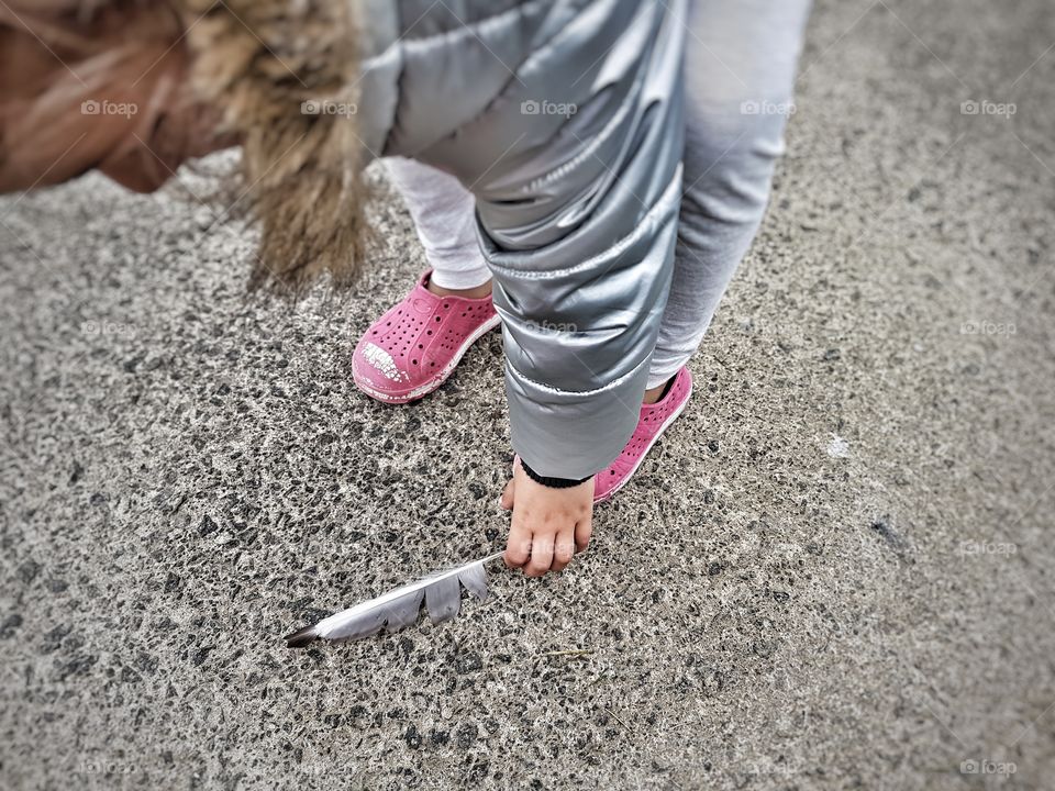 little girl finding a feather on the pavement