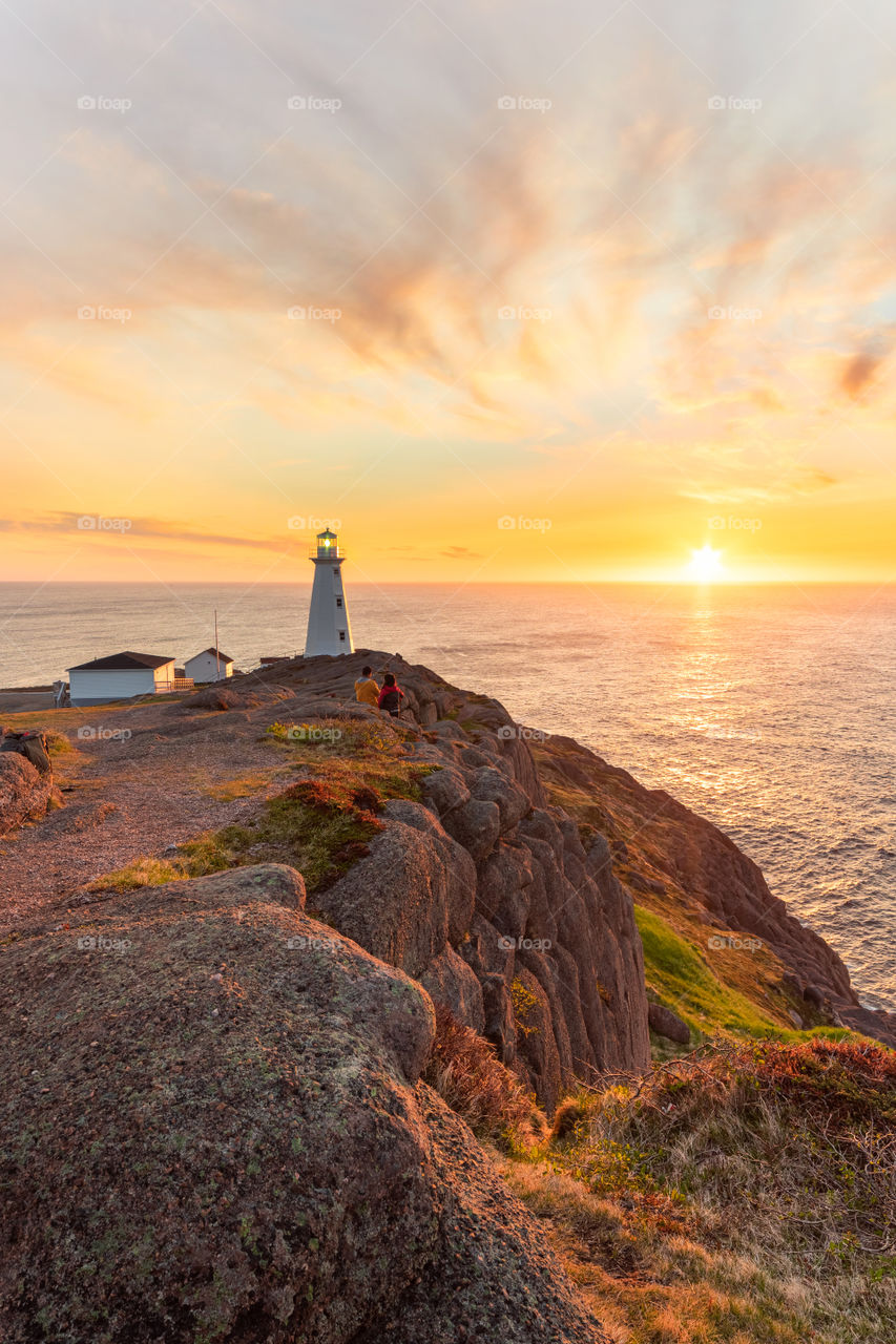 Sun rising over the horizon creating soft pastel colors, as a beautiful classic lighthouse sits on the edge of a cliff. 