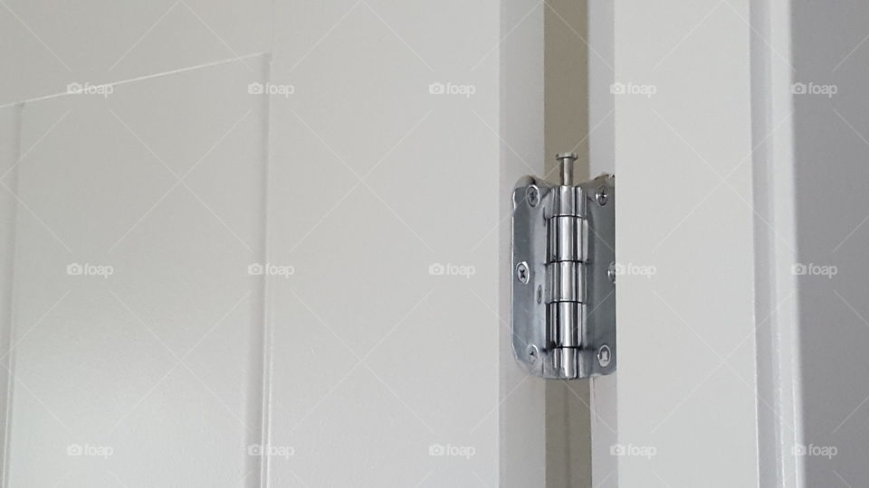 Silver modern door hinge closeup on white door.