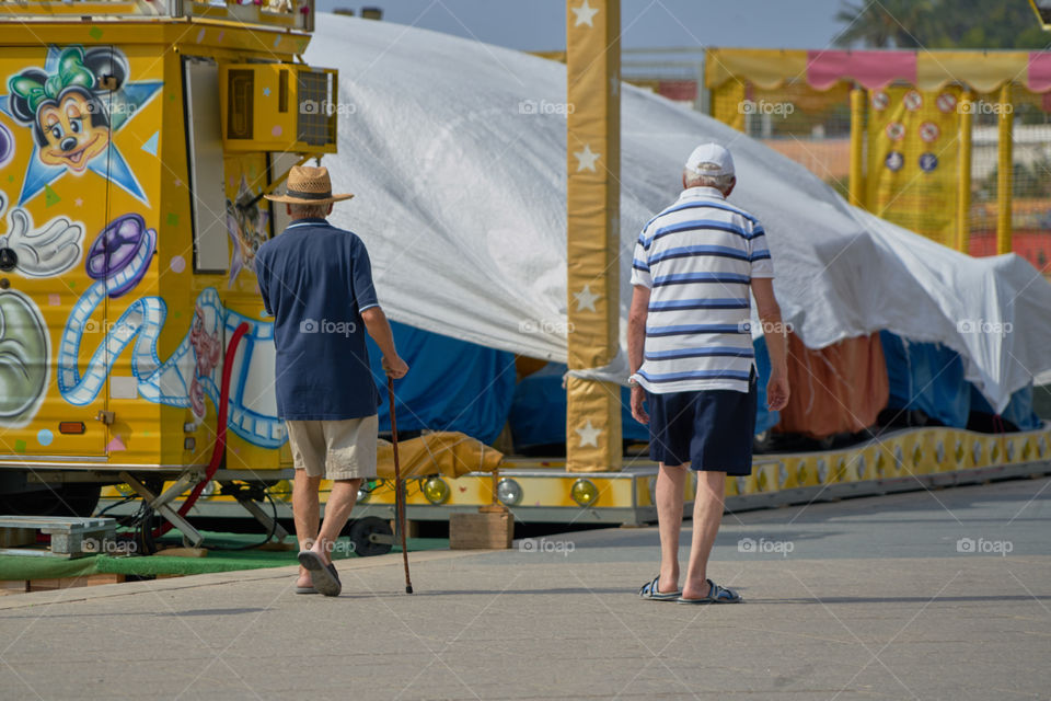 Ancianos paseando frente a unas atracciones infantiles.