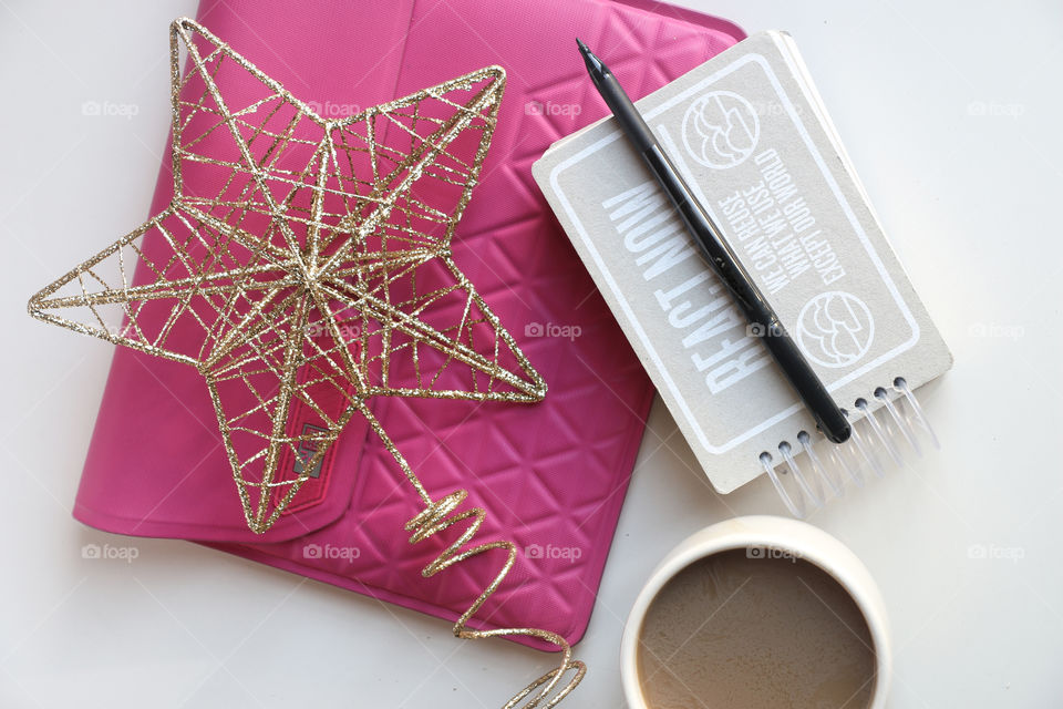 Overhead shot of a pink ipad bag, star shaped golden christmas ornament, gray notebook, black pen.